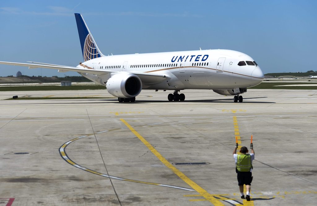 Un avión Boeing 787 Dreamliner de United Airlines estacionado en una pista de aeropuerto con un trabajador de servicios de rampa en primer plano.