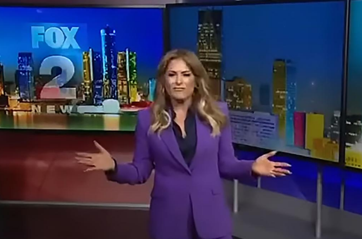 A female news presenter wearing a purple blazer stands at a desk in a television studio with a cityscape and Fox 2 News branding visible in the background.