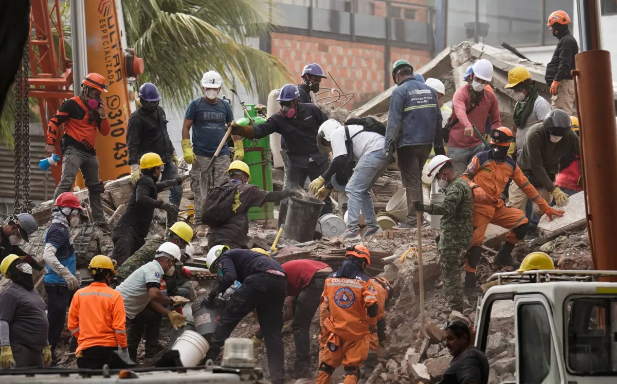 Equipo de rescate y trabajadores con cascos de protección trabajando entre escombros y ruinas en un sitio de desastre.