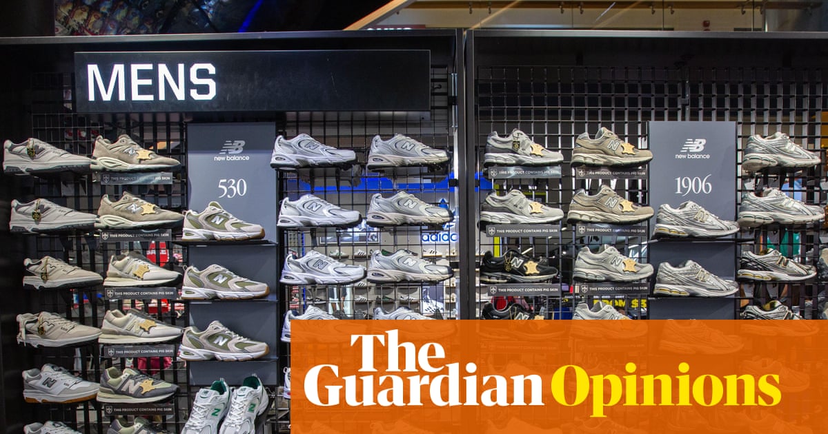 The window display of a JD Sports store shows multiple pairs of white and cream-colored sneakers from New Balance and other brands arranged on shelves, with a "MENS" sign visible above.
