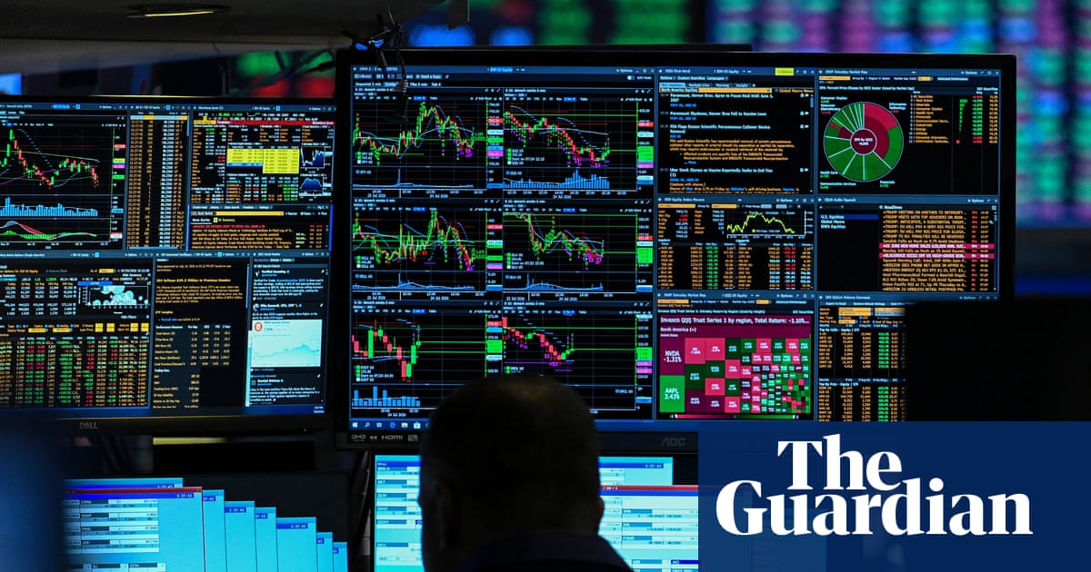 A trader is silhouetted against multiple computer monitors displaying colorful stock market charts, financial data tables, and trading information with green and red indicators.