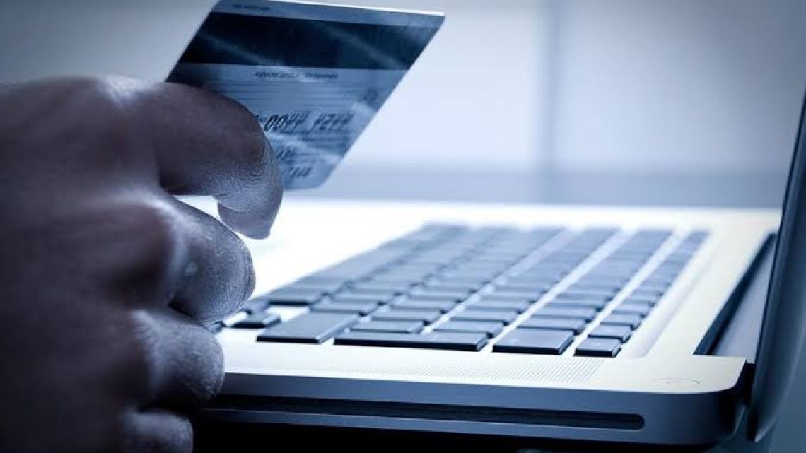 A gloved hand holds a credit card over a laptop keyboard, representing a digital transaction or online fraud.