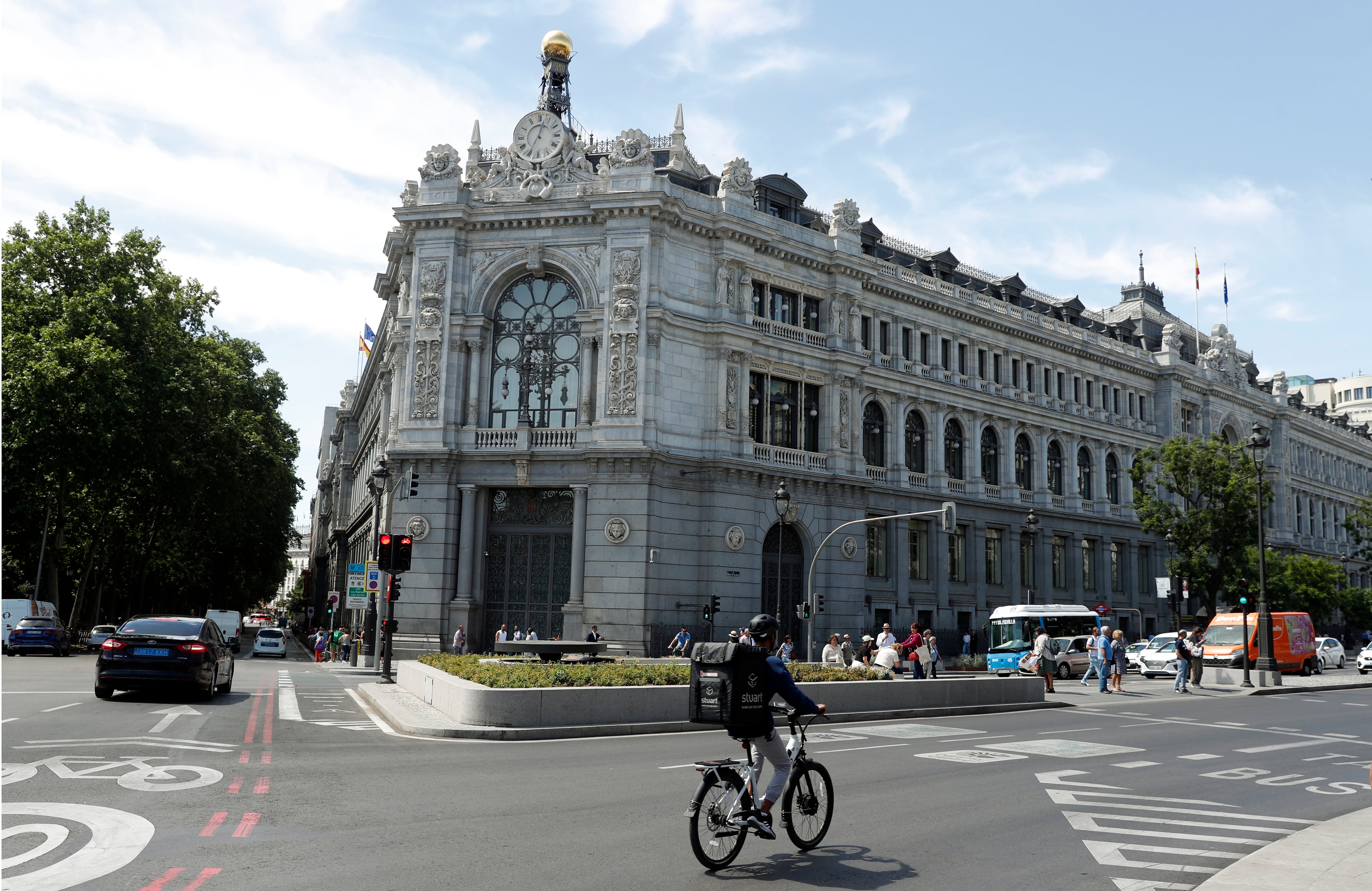 Un ciclista cruza una plaza frente a un edificio histórico de piedra blanca con torres, relojes y una cúpula dorada en una ciudad europea.