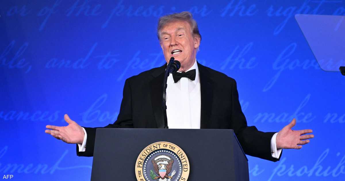 Un hombre en esmoquin con pajarita habla desde un podio con el sello presidencial de Estados Unidos, con los brazos extendidos, frente a un fondo azul.