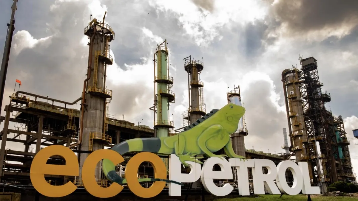 Un letrero con el logo de Ecopetrol frente a una refinería con múltiples torres de destilación y estructuras industriales bajo un cielo nublado.