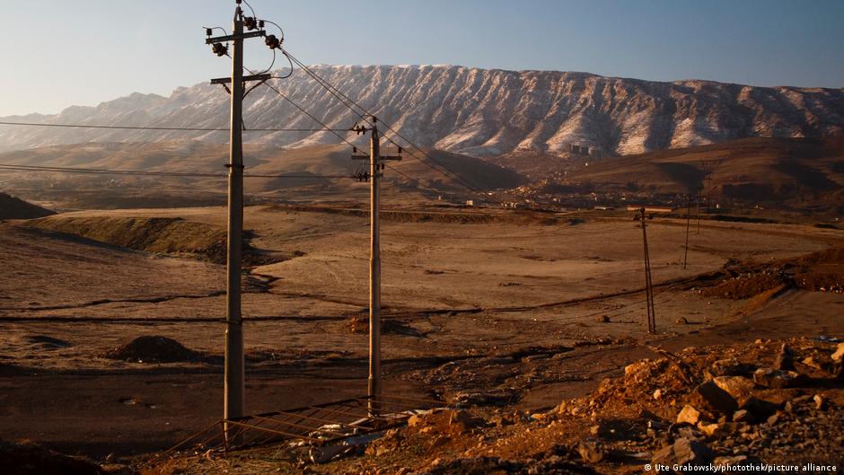 Poste de servicios eléctricos con cables en un terreno árido y desértico con montañas áridas al fondo bajo luz dorada.