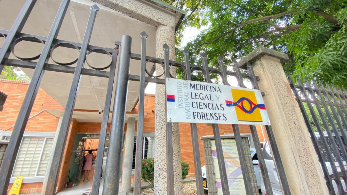 A sign reading "Instituto Nacional de Medicina Legal y Ciencias Forenses" mounted on a metal gate at the entrance of a brick building.