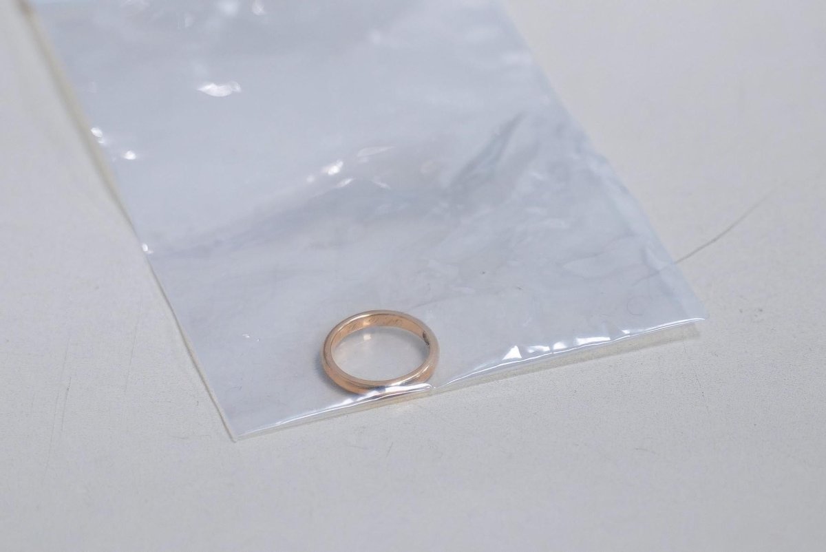 A gold wedding ring rests inside a clear plastic bag on a white surface.