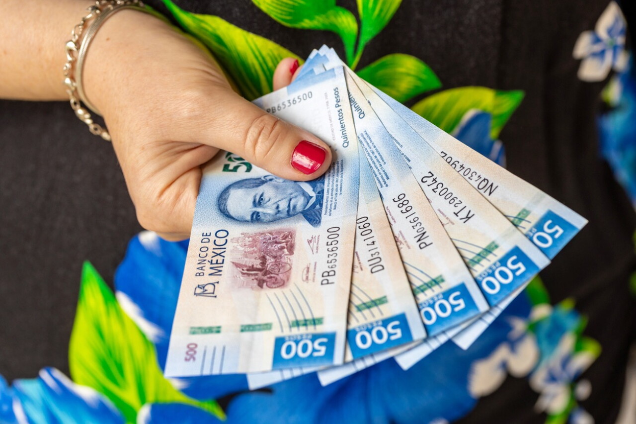 Una mano con las uñas pintadas de rojo sostiene varios billetes mexicanos de 500 pesos desplegados como abanico.