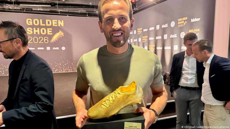 A man holds a golden football boot in his hands while smiling in front of a backdrop at the 2026 Golden Boot awards ceremony.