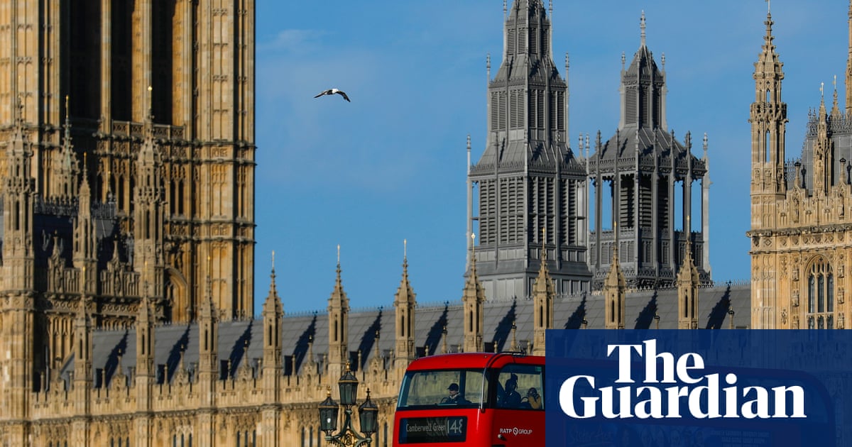 A red double-decker bus passes in front of the Houses of Parliament and other Gothic Revival buildings in London under a clear blue sky.
