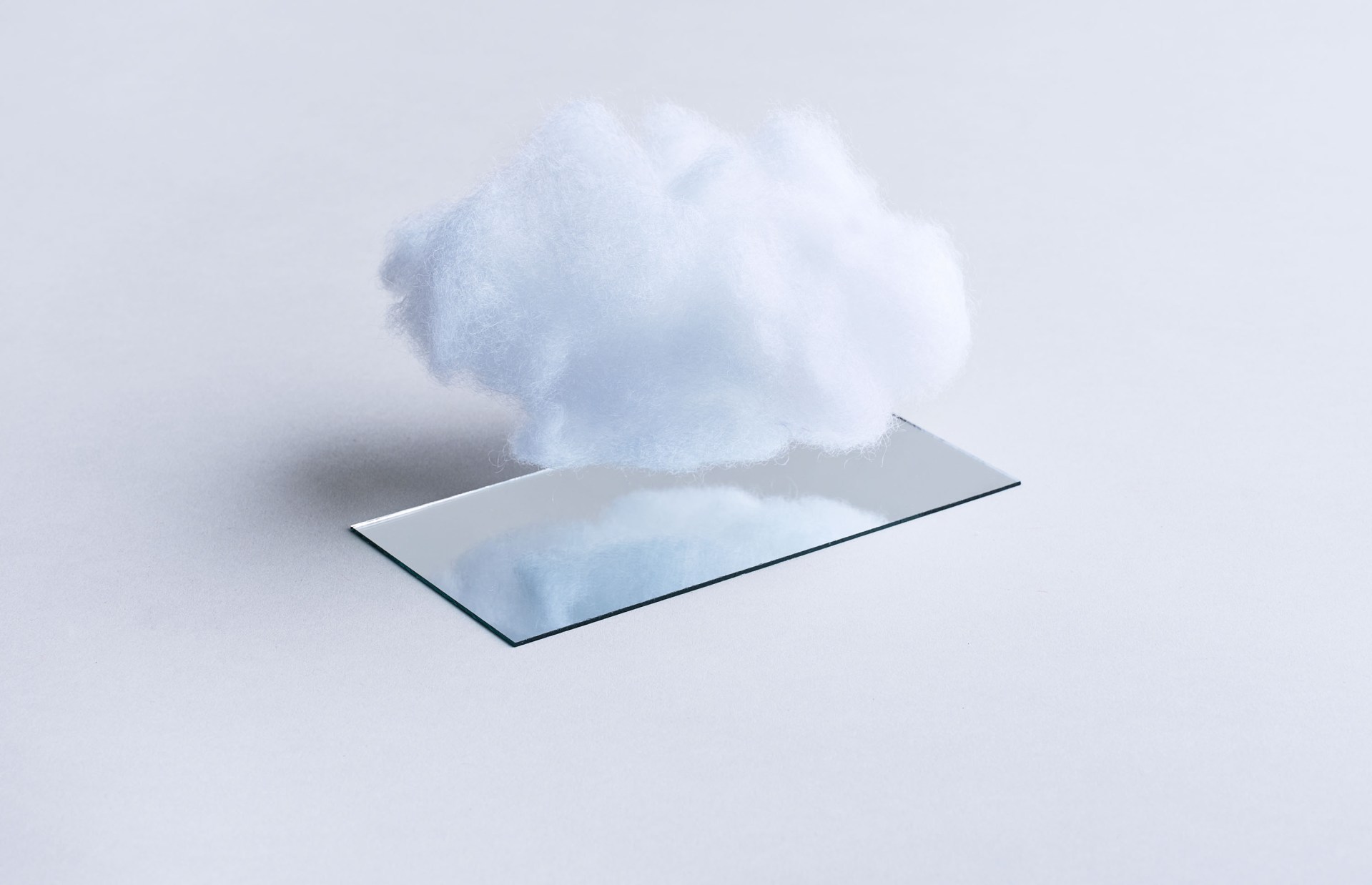 A fluffy white cloud emerges from a flat glass or transparent rectangular panel against a light gray background.