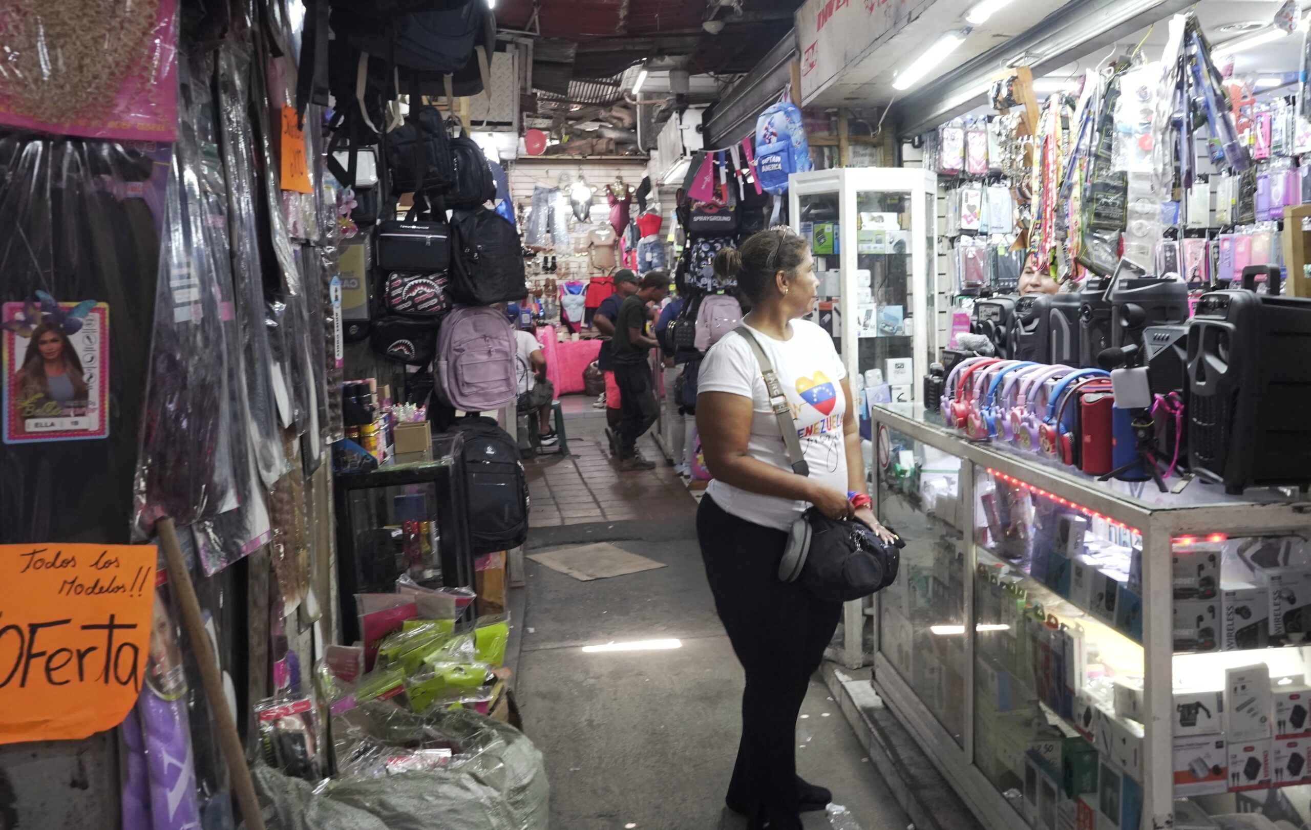 Interior of a small commercial shop showing clothing racks, merchandise displays, and a few shoppers browsing in narrow aisles.