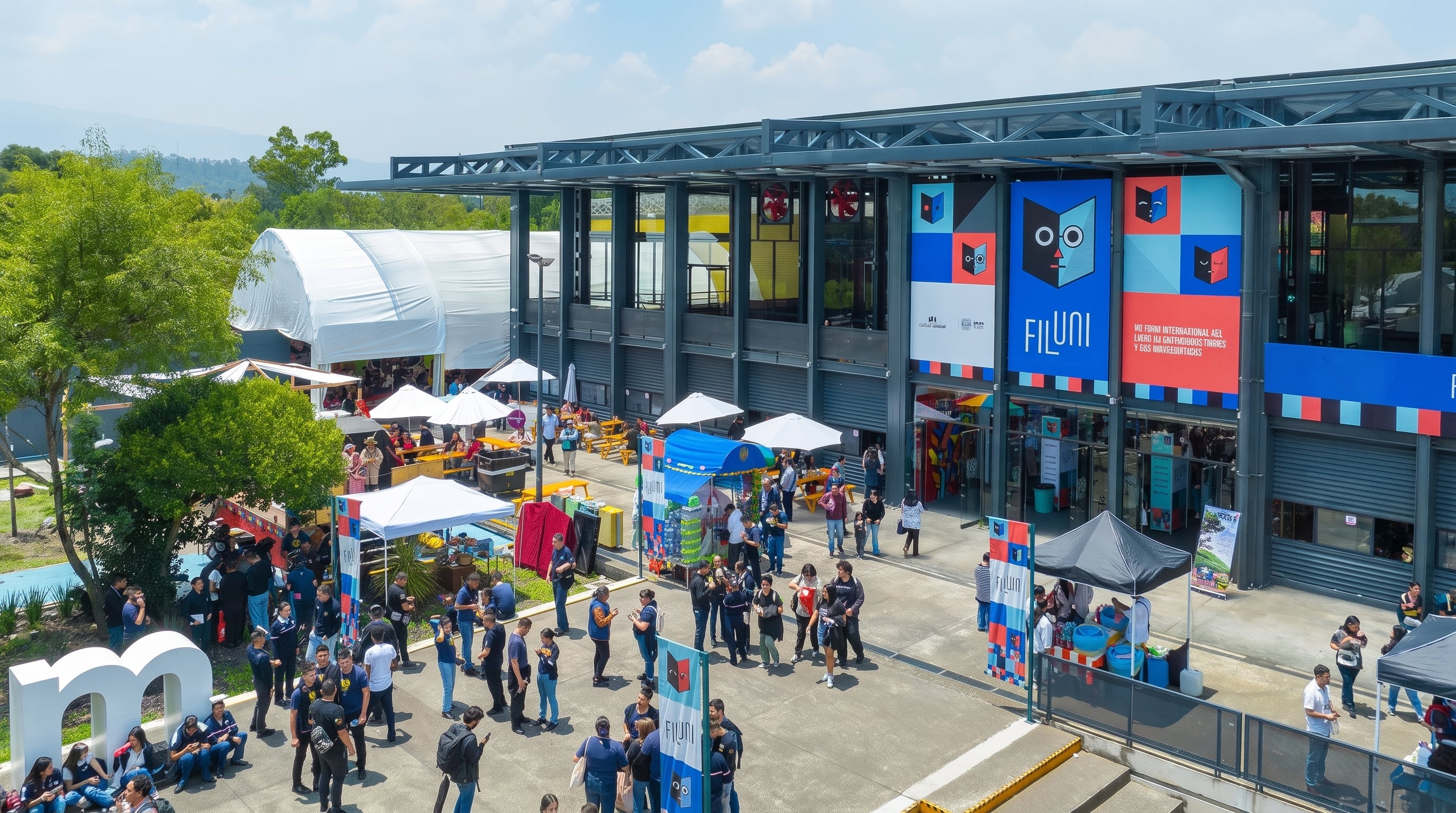 An outdoor event with multiple visitors gathered in an area with white tents, surrounded by a modern building with metallic structure and red, blue and white panels showing the FILUNI logo.