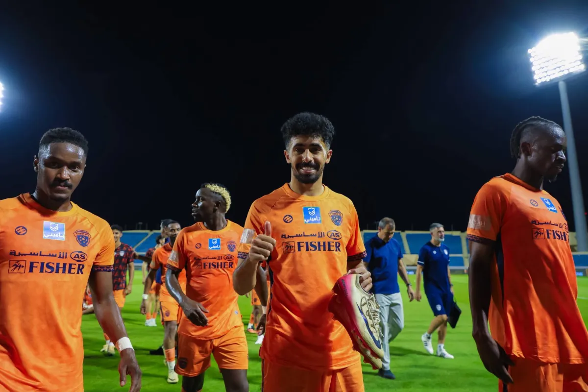 Football players in orange kit walk on the pitch of a night-lit stadium.