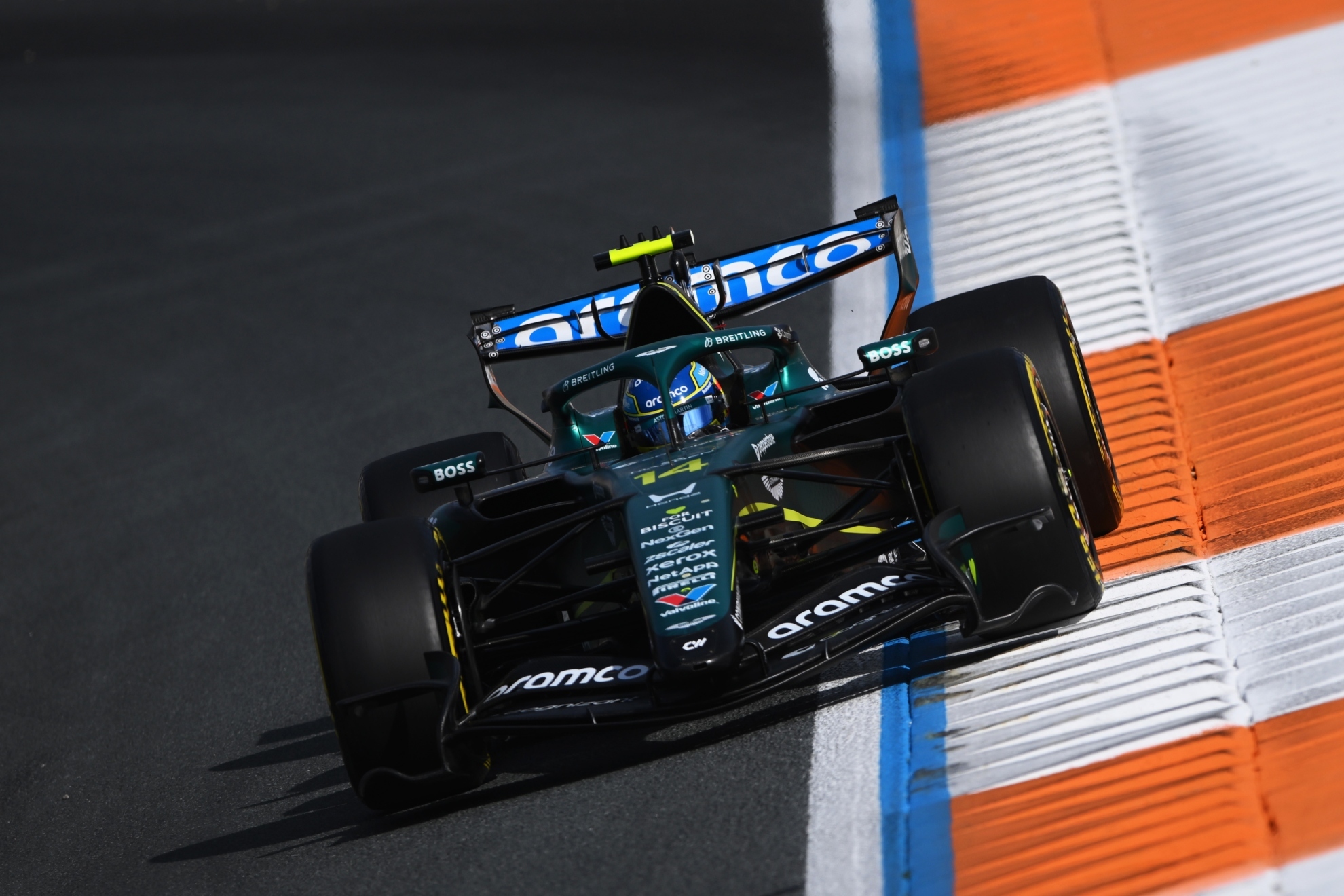 Un monoplaza de Fórmula 1 de color negro y azul con patrocinadores Aston Martin y Aramco circula por una pista de carreras con bordillos azules, blancos y naranjas.