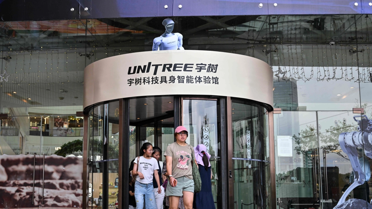 Una tienda de exhibición de Unitree Robotics con un robot humanoide de color azul posicionado en la parte superior, mientras varias personas entran y salen del establecimiento.