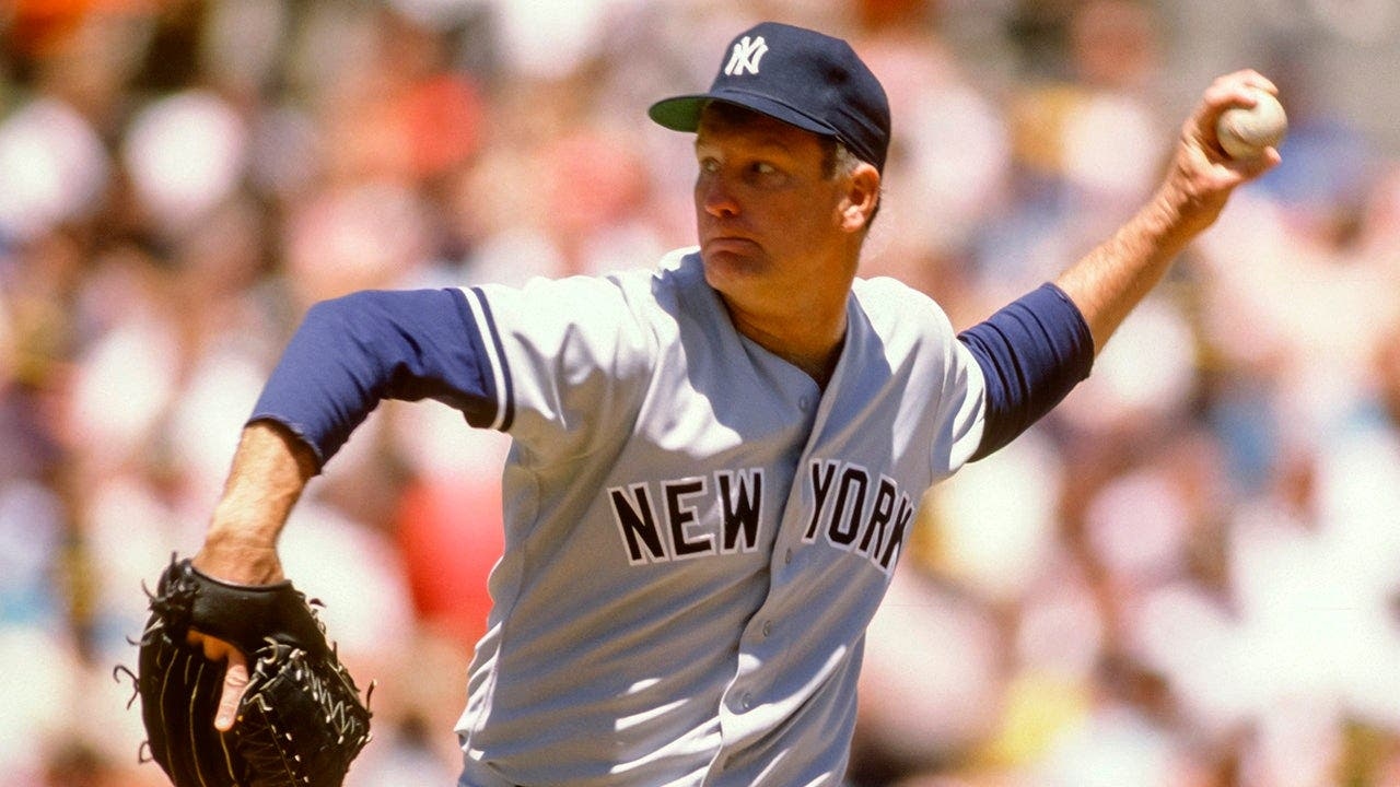 A pitcher for the New York Yankees in throwing position during a game, arm extended and ball in hand.