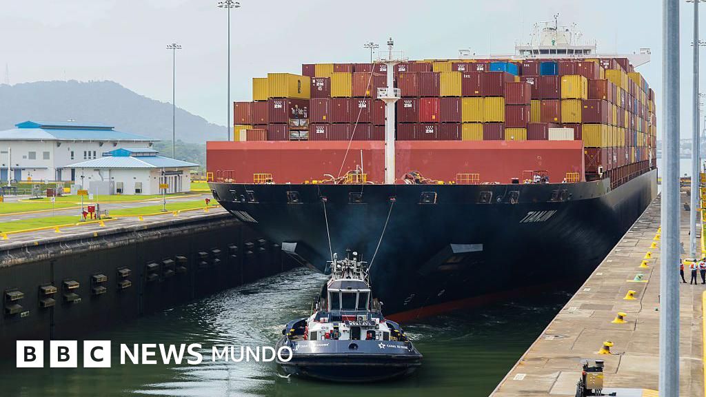 Un buque portacontenedores de gran tamaño cargado con contenedores rojos y amarillos siendo remolcado por un remolcador en una esclusa del Canal de Panamá.