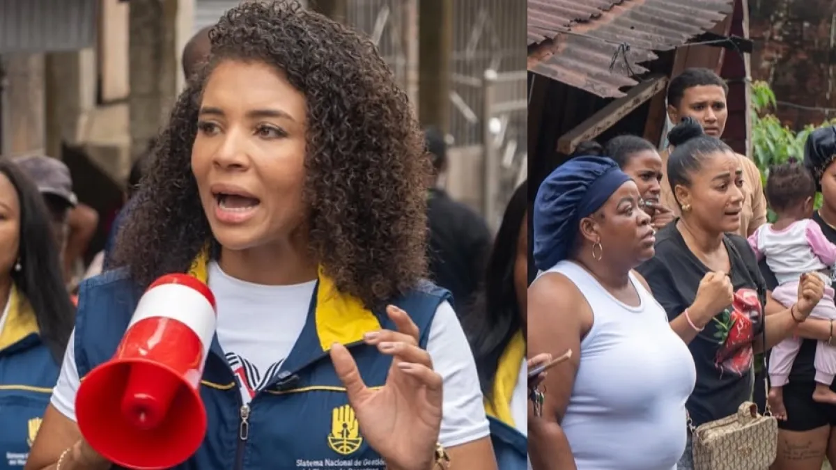 A woman with curly hair, wearing a blue and yellow institutional vest with logo, holds a red megaphone while speaking to a group of people on a street.