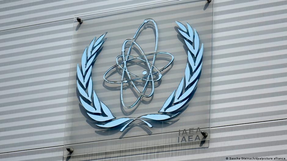 El logo de la Agencia Internacional de Energía Atómica (AIEA) con las letras y un símbolo de átomo, montado en una pared de vidrio rayado.