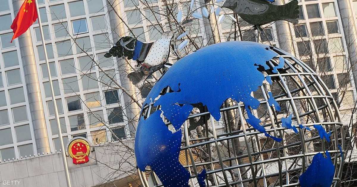 A blue globe sculpture with embossed continents, surrounded by bare branches, with an office building in the background and the Chinese national flag visible on the left.