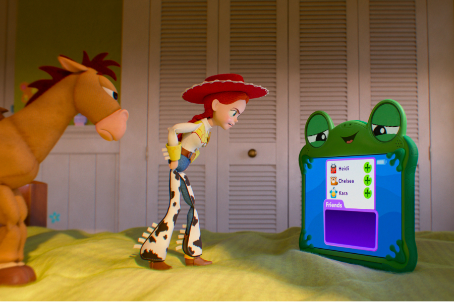 Three animated characters from Toy Story stand in a room: an orange horse with red hair on the left, a cowgirl named Jessie in the center wearing a red cowboy hat and spotted vest, and a green frog device displaying a friends list on the right.