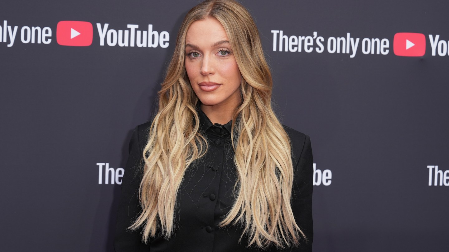 A woman with long, wavy blonde hair wearing a black blazer at a media event.