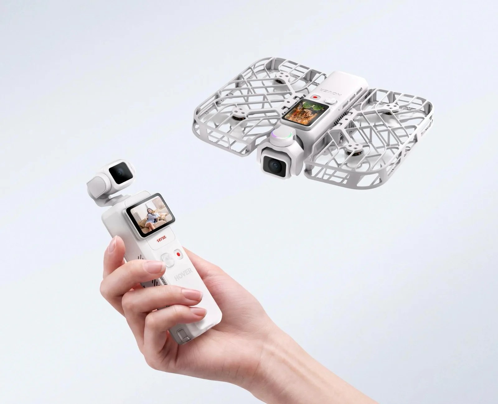 A hand holds a small white device with a touchscreen and camera, while two white square drones with propellers are shown in the background.