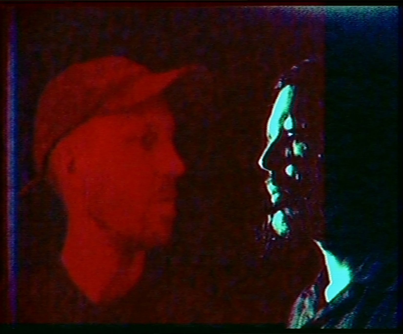 A thermal or infrared image showing a person in profile on the right side with bright cyan highlights against a dark background, with a large red shape on the left side.