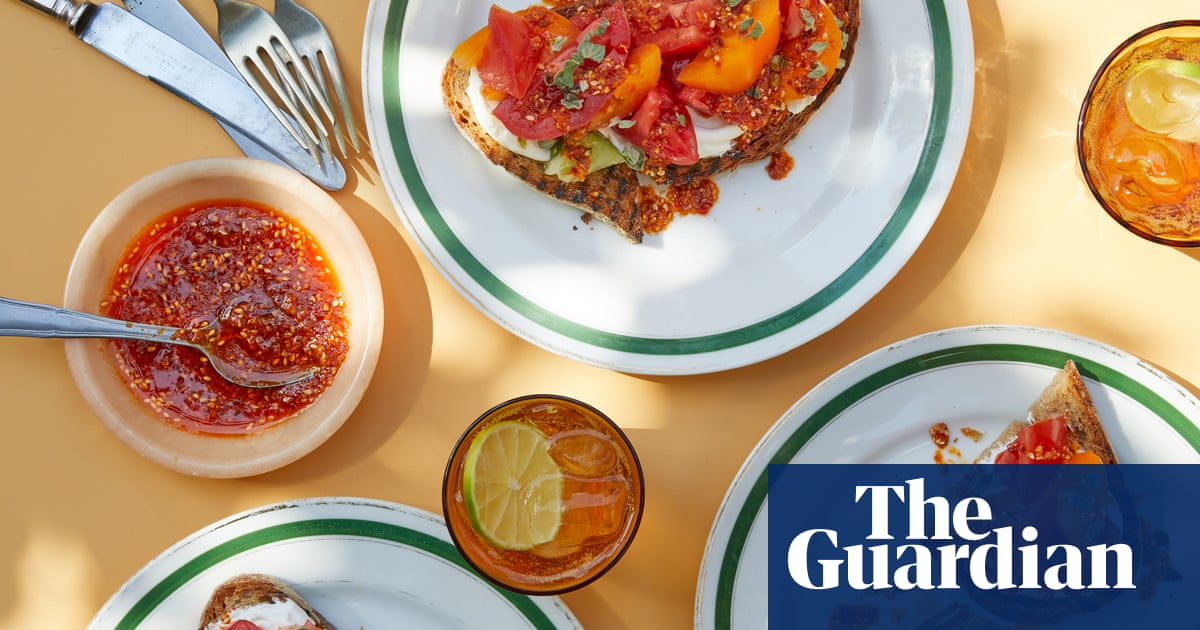 Several open toasts with fresh tomato, vegetables and white cheese on white plates with green trim, accompanied by iced drinks and a cup with red sauce.