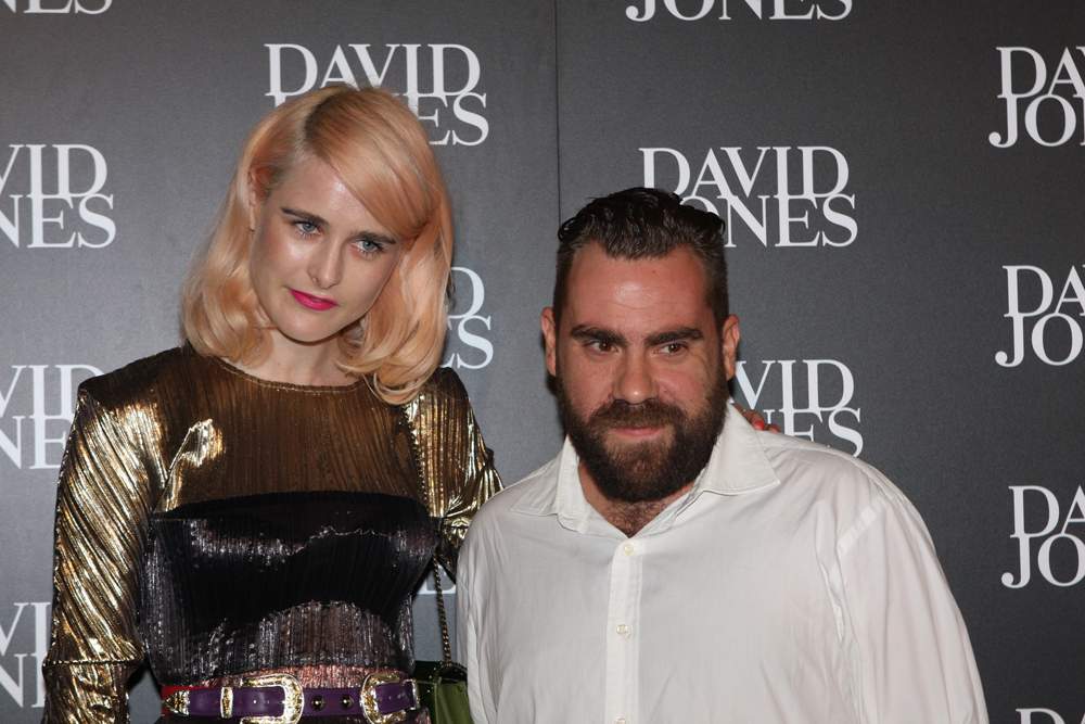 A woman with blonde hair wearing a gold and black sequined dress stands next to a man with a dark beard wearing a white button-up shirt at a David Jones event.