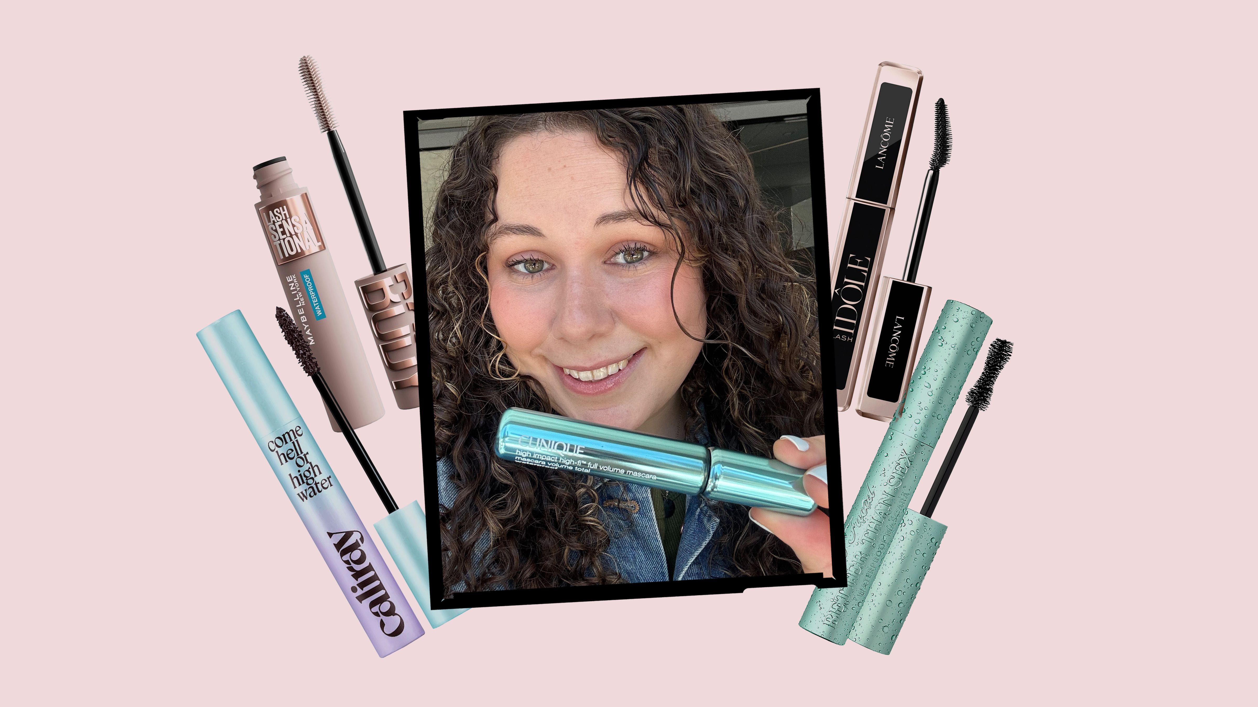 A smiling young woman with dark curly hair holds a turquoise blue mascara while surrounded by different mascara products on a light pink background.
