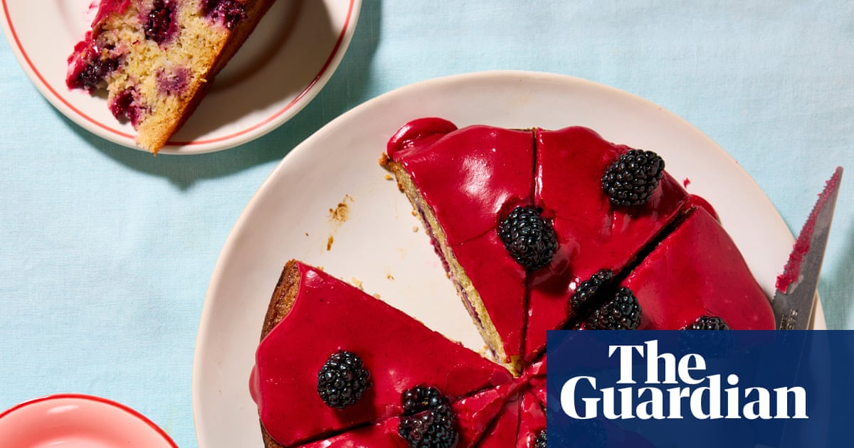 Two slices of almond cake with red glaze and fresh blackberries on white plates against a light blue background.