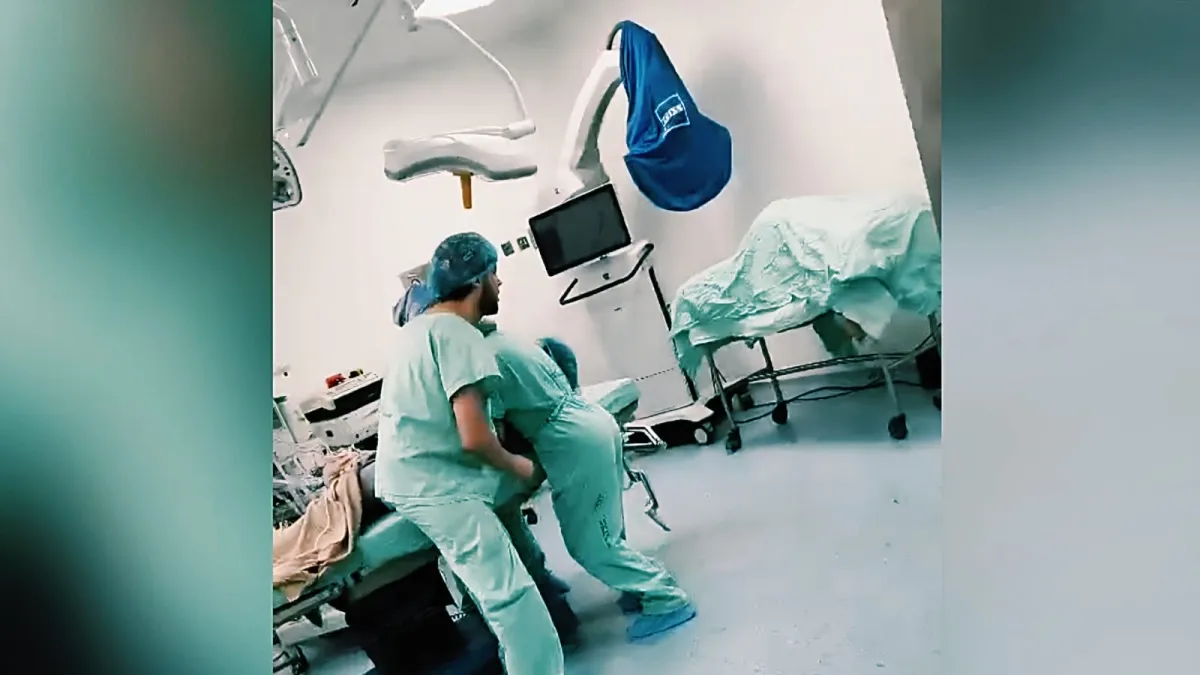 Una anestesióloga vestida con uniforme quirúrgico verde y mascarilla protectora cubre el cuerpo de un paciente en una camilla de cirugía durante un terremoto en un quirófano.