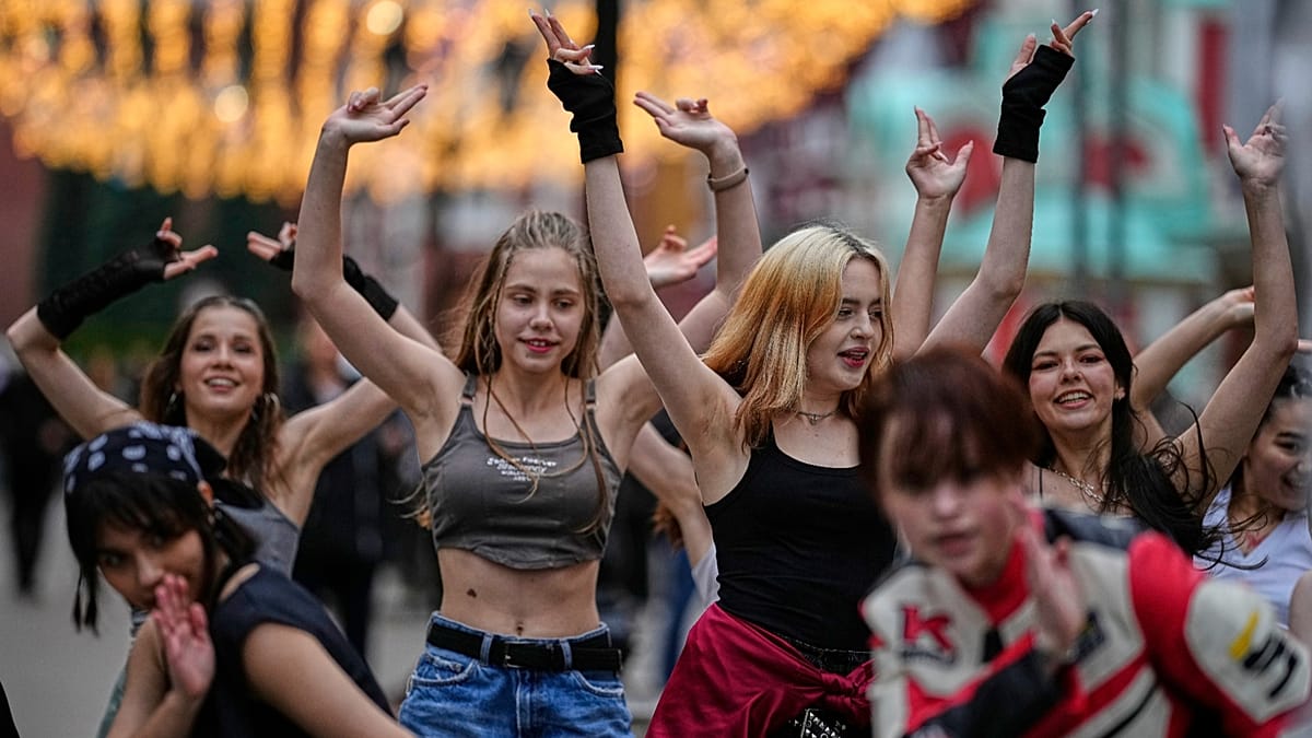 Un grupo de jóvenes con los brazos levantados hacen gestos y poses en una calle, mientras otros los observan en el fondo.