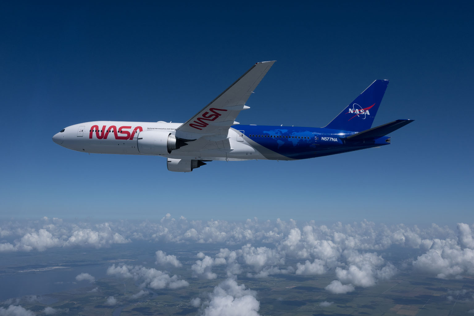 A Boeing 777 aircraft with NASA inscribed on its white fuselage flies above a layer of clouds, displaying its new dark blue and white paint scheme.
