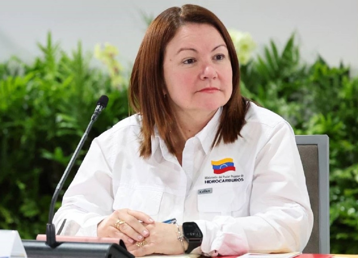 A woman with reddish-brown hair wearing a white official uniform with the Venezuelan flag and "Hydrocarbuels" insignia sits at a desk with a microphone, looking toward the side.